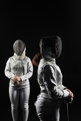 Fototapeta na wymiar two women wearing helmets and white uniforms fencing on black background