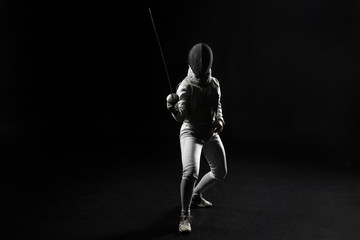 full length of female fencer in uniform posing with sword on black background