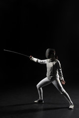 full length of female fencer in uniform posing with sword on black background