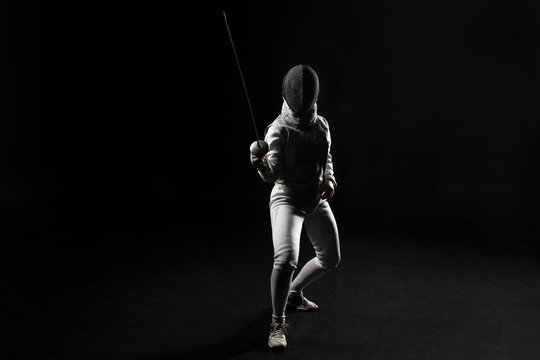 Full Length Of Female Fencer In Uniform Posing With Sword On Black Background