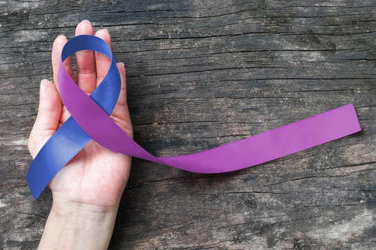 Blue purple ribbon on human hand aged wood background for RA rheumatoid arthritis illness disease