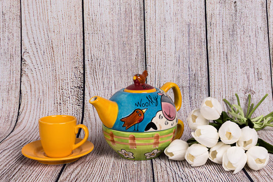 Tetera decorada, taza de té amarilla y tulipanes blancos.