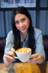 Pretty young barista is offering cup of coffee in a cafe. Blurred background.
