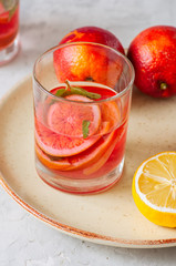 Refreshing blood orange water or infused water in a glass on a white stone background