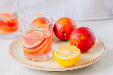Refreshing blood orange water or infused water in a glass on a white stone background