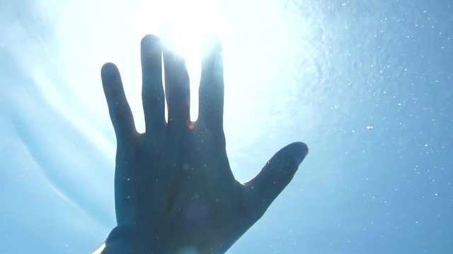 Underwater view of hand in sun rays shining