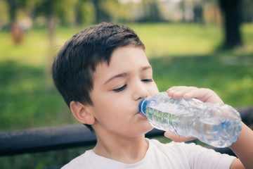 Small kid refreshing himself with water from plastic bottle.