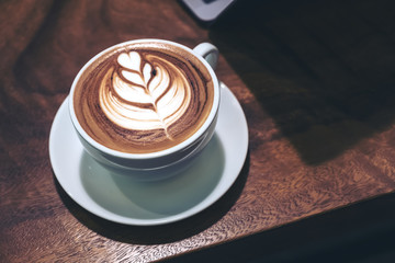 Closeup image of a cup of hot latte coffee with heart latte art  and laptop on wooden table