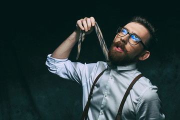 Young stylish hipster businessman or manager holds his necktie in hand as if he decided to hang himself on it conceptually showing high level of stress and overwork.