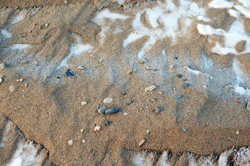 Background of stones on the sand beach covered with snow in winter on the sunset by the lake Baikal, Siberia, Russia