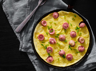 fried eggs omelette with sausage in a frying pan on wooden table
