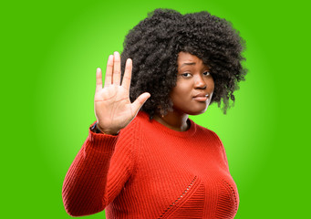 Beautiful african woman annoyed with bad attitude making stop sign with hand, saying no, expressing...