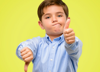 Handsome toddler child with green eyes confused with thumbs up and down, trying to take a decision...