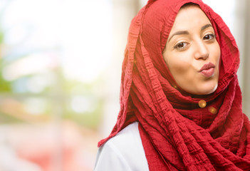 Young arab woman wearing hijab expressing love, blows kiss at camera, flirting