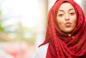 Young arab woman wearing hijab expressing love, blows kiss at camera, flirting