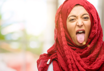 Young arab woman wearing hijab sticking out tongue at camera at sign of disobedience, protest and disrespect