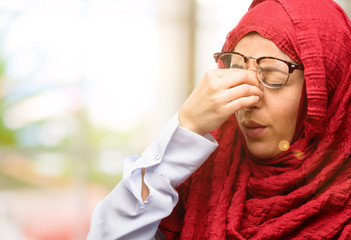 Young arab woman wearing hijab with sleepy expression, being overworked and tired, rubbes nose because of weariness
