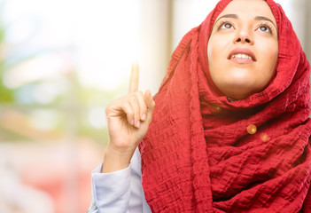 Young arab woman wearing hijab happy and surprised cheering pointing up