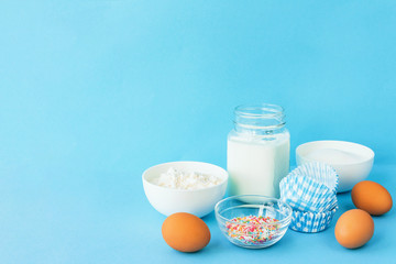 Eggs of chicken, flour in a bowl, sugar, milk in a glass jar whisk ingredient for cooking a bake on a blue background with copy space