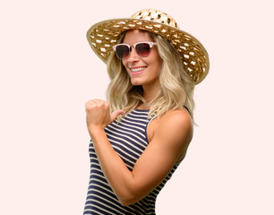 Young woman using sunglasses wearing summer hat proud, excited and arrogant, pointing with victory face