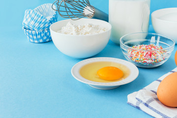 Eggs of chicken, flour in a bowl, sugar, milk in a glass jar whisk ingredient for cooking a bake on a blue background with copy space
