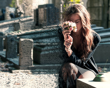 Sad woman holding bunch of flowers near a grave - Dispersion effect
