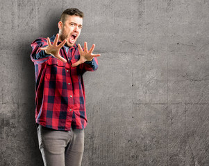 Young handsome man disgusted and angry, keeping hands in stop gesture, as a defense, shouting