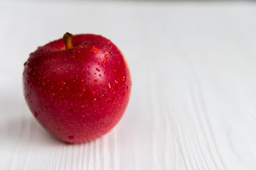 Single red apple on white wooden surface close