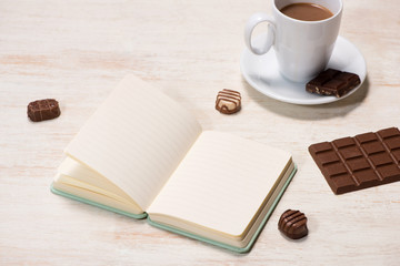 Coffee milk cup and delicious chocolates with notebook on table.