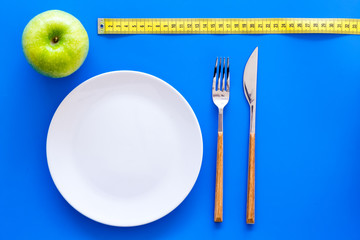 Proper nutrition with dietary fibre for weight loss. Apple on plate near measuring tape on blue background top view mockup