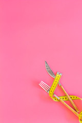 Proper nutrition for slimming. Fork and knife with wound measuring tape on pink background top view copy space