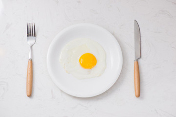 Top view of white dish with fried egg on white background.