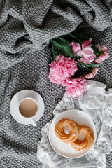 A cup of coffee with sweets and peonies on a gray background