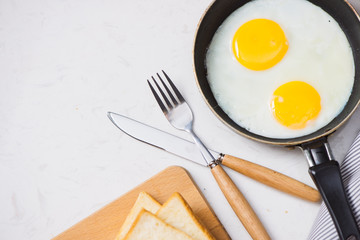 Eating in the process, fried eggs in a frying pan, toast  and orange juice for breakfast on a white background. Daylight.