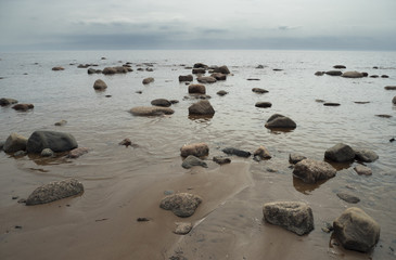 Sea waves splashing on the shore. Granite stones on a sandy beach.