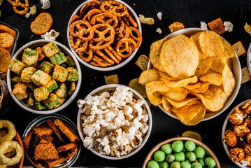 Variation different unhealthy snacks crackers, sweet salted popcorn, tortillas, nuts, straws, bretsels, back chalkboard copy space