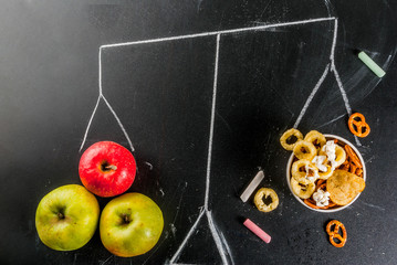 Fototapeta na wymiar Healthy and unhealthy snack concept with crackers, chips and apples on black chalkboard