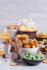 Variation different unhealthy snacks crackers, sweet salted popcorn, tortillas, nuts, straws, bretsels, white marble background copy space