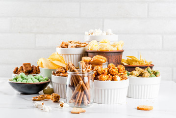 Variation different unhealthy snacks crackers, sweet salted popcorn, tortillas, nuts, straws, bretsels, white marble background copy space