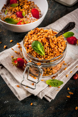 Homemade granola from mix of cereals (barley, oat, rye, bran) with with strawberry, mint leaves and fresh organic milk on dark blue concrete background
