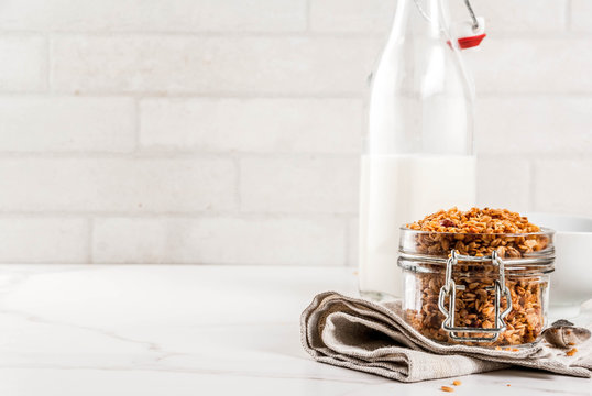 Homemade granola from mix of cereals (barley, oat, rye, bran) with dry fruits, nuts, with fresh organic milk on white marble background