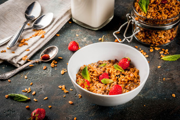Homemade granola from mix of cereals (barley, oat, rye, bran) with with strawberry, mint leaves and fresh organic milk on dark blue concrete background