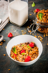 Homemade granola from mix of cereals (barley, oat, rye, bran) with with strawberry, mint leaves and fresh organic milk on dark blue concrete background