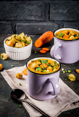 Homemade pureed carrot cream soup, with bread crackers, fresh herbs and cream. On a dark blue background,