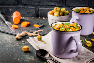 Homemade pureed carrot cream soup, with bread crackers, fresh herbs and cream. On a dark blue background,