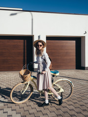 Pretty girl in hat and dress by cruiser bicycle in suburb