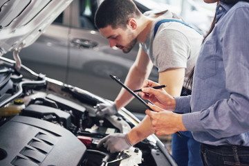 A man mechanic and woman customer look at the car hood and discuss repairs