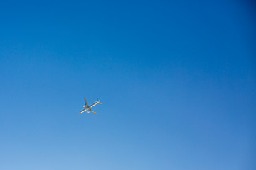 Passenger airplane flies overhead on clear blue sky background with no clouds. Bottom view