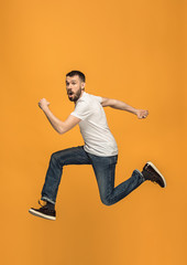Fototapeta na wymiar Freedom in moving. handsome young man jumping against orange background