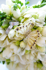 A wedding bouquet of white freesias with a decorative butterfly and silver wedding rings. 